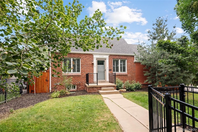 view of front facade with a front lawn, a shingled roof, fence, and brick siding