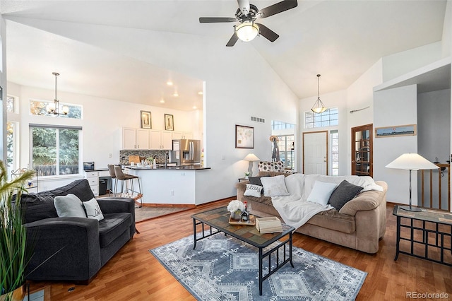 living room with plenty of natural light, high vaulted ceiling, ceiling fan with notable chandelier, and light hardwood / wood-style flooring