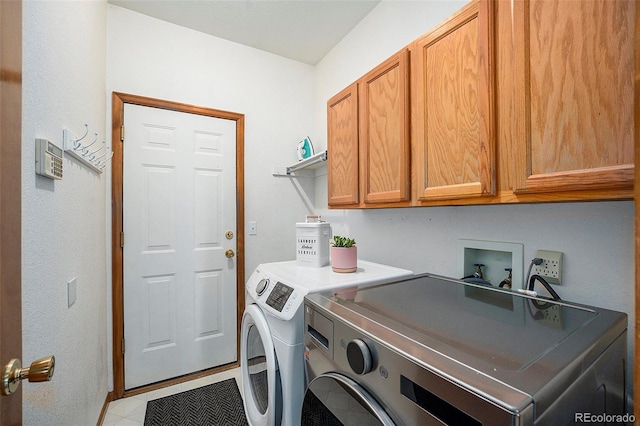 clothes washing area with washing machine and clothes dryer, light tile patterned floors, and cabinets