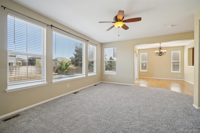 carpeted empty room featuring ceiling fan with notable chandelier