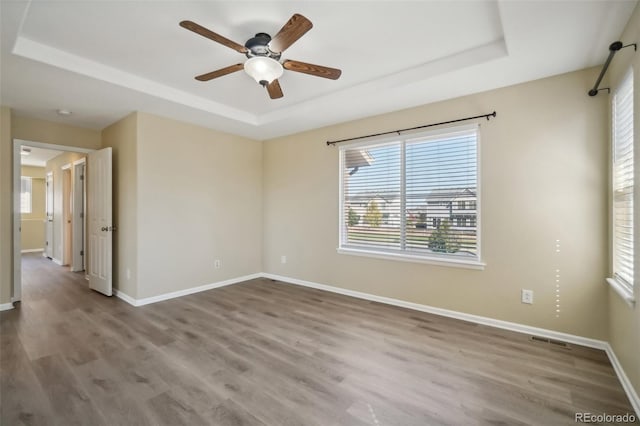 empty room featuring hardwood / wood-style floors, ceiling fan, and a raised ceiling