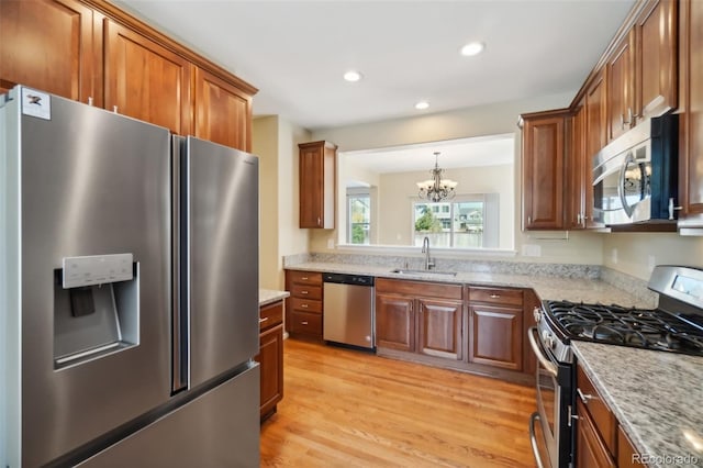 kitchen featuring light stone countertops, light wood-type flooring, stainless steel appliances, sink, and an inviting chandelier