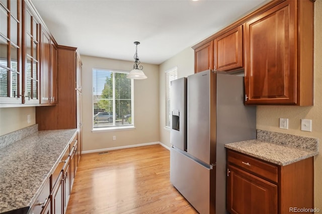 kitchen with decorative light fixtures, light stone counters, stainless steel fridge with ice dispenser, and light hardwood / wood-style flooring