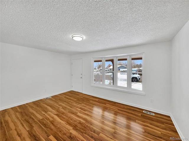 empty room featuring visible vents, a textured ceiling, baseboards, and wood finished floors