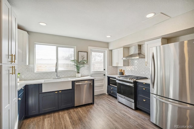 kitchen featuring wall chimney exhaust hood, sink, stainless steel appliances, hardwood / wood-style floors, and white cabinets