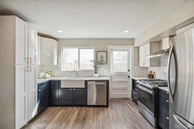 kitchen with sink, backsplash, stainless steel appliances, light hardwood / wood-style floors, and white cabinets