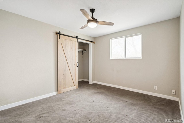 unfurnished bedroom with a barn door, carpet, ceiling fan, and a closet