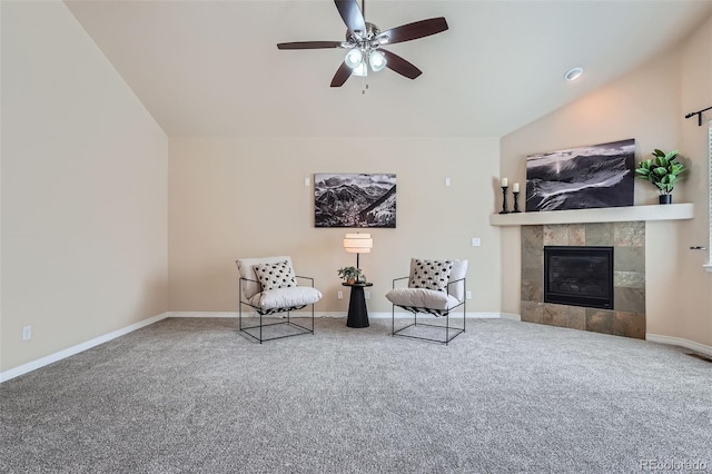 living area with vaulted ceiling, carpet floors, a tiled fireplace, and a ceiling fan