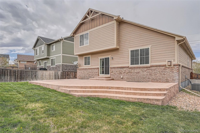 rear view of property featuring board and batten siding, a lawn, brick siding, fence, and entry steps