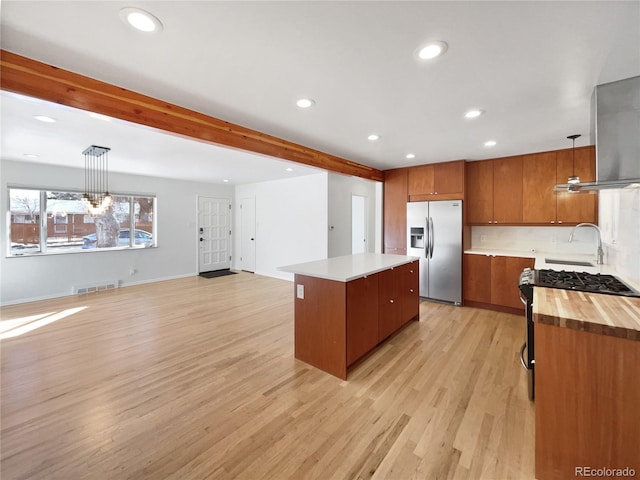 kitchen with appliances with stainless steel finishes, a center island, decorative light fixtures, beamed ceiling, and light wood-type flooring