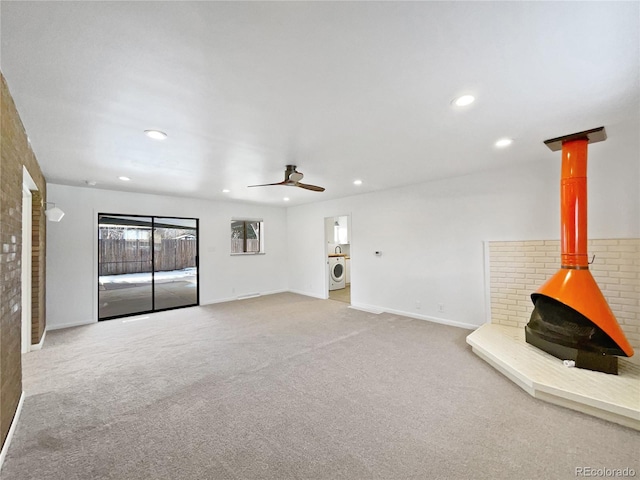 unfurnished living room with ceiling fan, a wood stove, washer / dryer, and carpet flooring