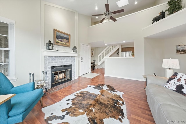 living room with ceiling fan, a fireplace, hardwood / wood-style floors, and a towering ceiling