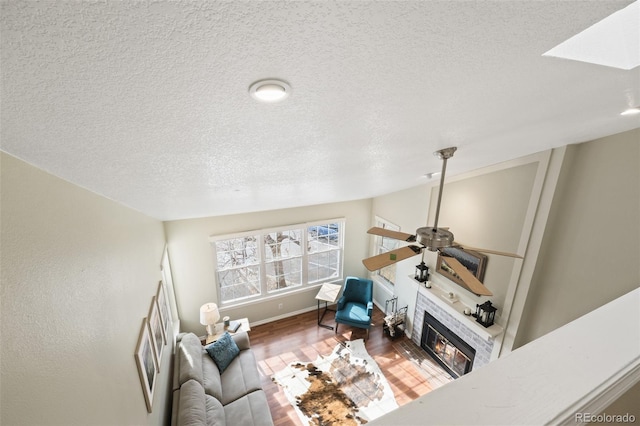 living room with a tiled fireplace, a textured ceiling, wood-type flooring, and ceiling fan