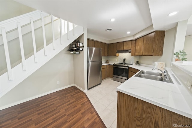 kitchen featuring sink, backsplash, stainless steel appliances, light stone countertops, and light wood-type flooring