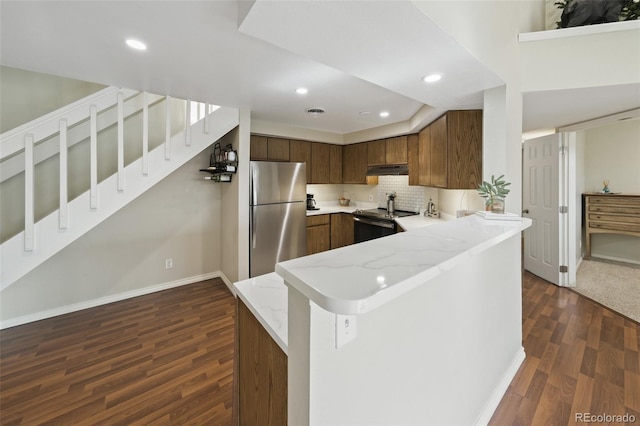 kitchen featuring light stone counters, appliances with stainless steel finishes, dark hardwood / wood-style flooring, kitchen peninsula, and decorative backsplash