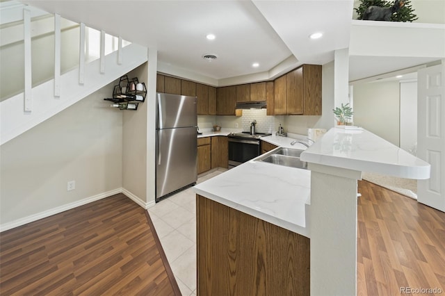 kitchen with stainless steel appliances, kitchen peninsula, sink, and light wood-type flooring