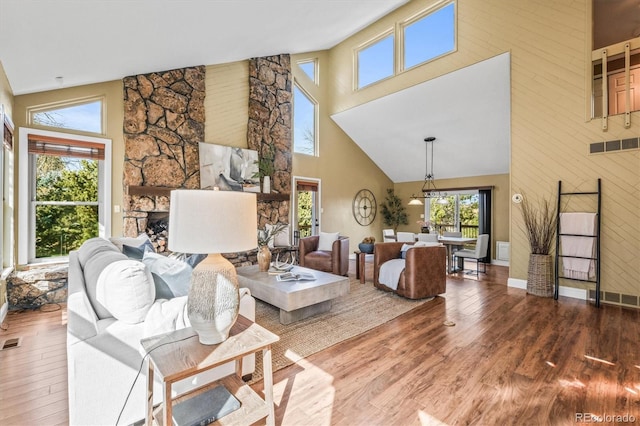 living room with visible vents, a fireplace, a towering ceiling, and wood finished floors