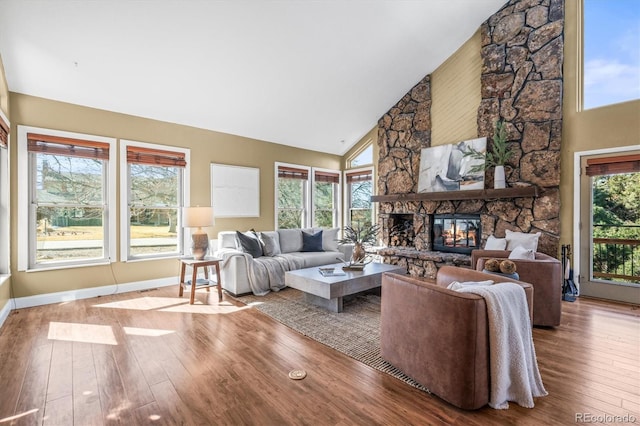 living room featuring high vaulted ceiling, a stone fireplace, wood-type flooring, and baseboards