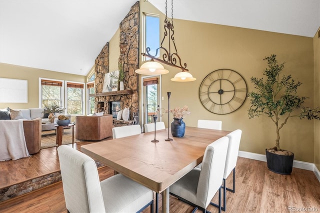 dining area featuring light wood-style floors, a fireplace, baseboards, and high vaulted ceiling