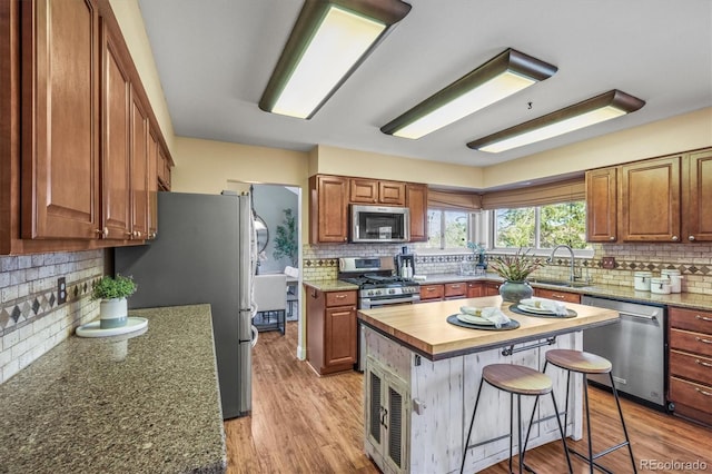 kitchen featuring a center island, appliances with stainless steel finishes, brown cabinetry, a sink, and light wood-type flooring