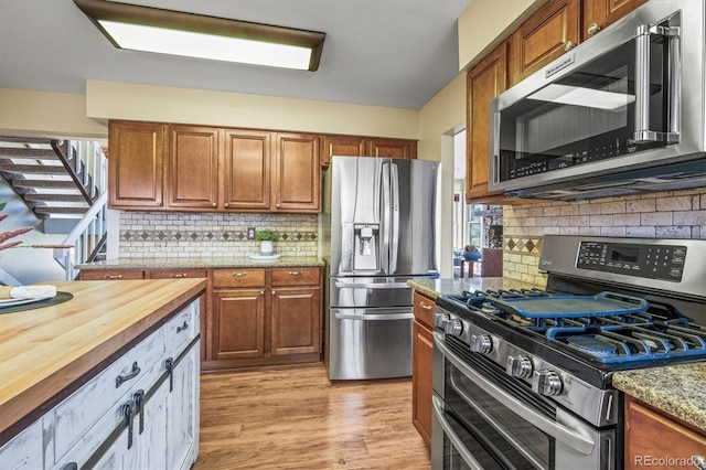 kitchen with light wood-style flooring, butcher block countertops, appliances with stainless steel finishes, and brown cabinets