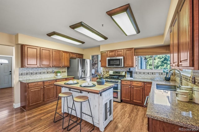 kitchen featuring appliances with stainless steel finishes, light stone counters, wood finished floors, a center island, and a sink