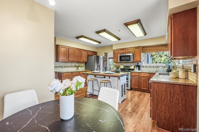 kitchen with stainless steel appliances, a sink, a kitchen island, light wood finished floors, and brown cabinetry