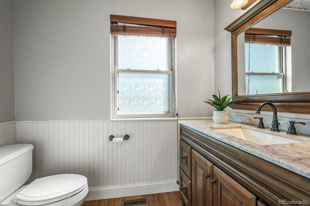 half bathroom with toilet, wood finished floors, vanity, visible vents, and wainscoting