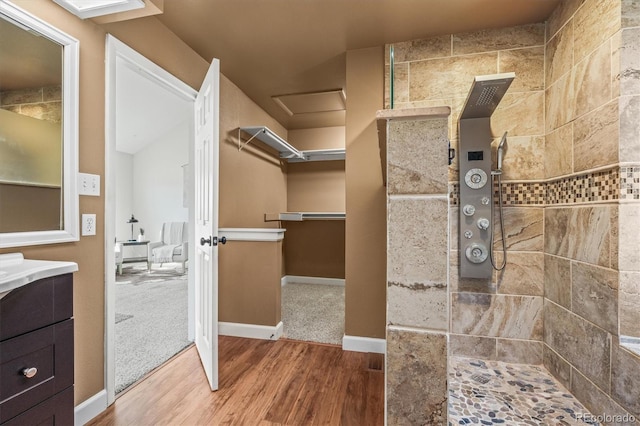 full bathroom with wood finished floors, vanity, baseboards, a walk in closet, and walk in shower