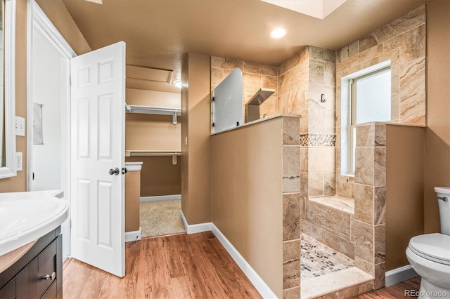 bathroom with toilet, wood finished floors, vanity, baseboards, and walk in shower