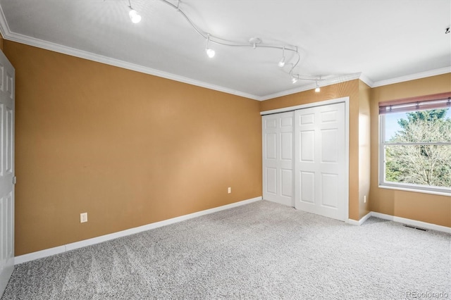 unfurnished bedroom with carpet floors, a closet, rail lighting, ornamental molding, and baseboards