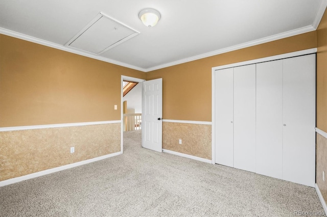 unfurnished bedroom featuring carpet, a closet, attic access, ornamental molding, and wainscoting