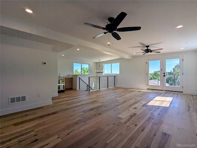 unfurnished living room featuring beam ceiling, french doors, wood-type flooring, and ceiling fan with notable chandelier