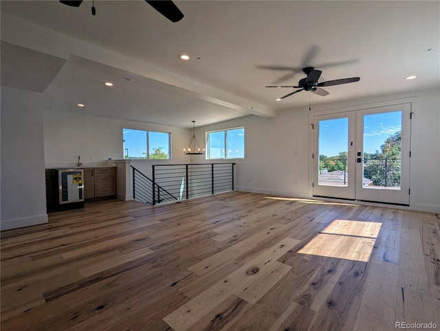 unfurnished living room with beam ceiling, ceiling fan with notable chandelier, and hardwood / wood-style flooring