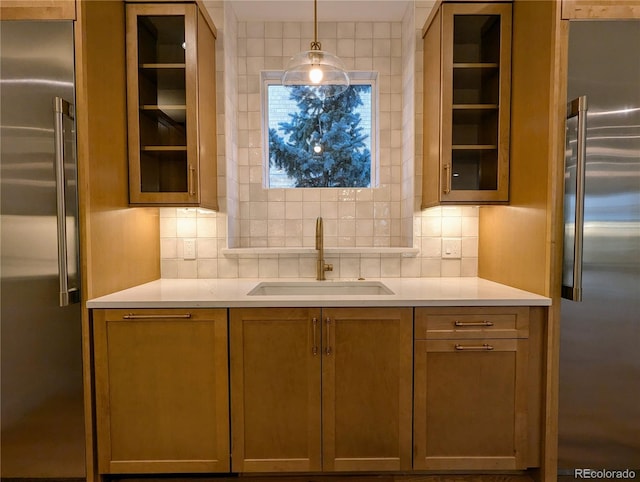 kitchen with decorative backsplash, high end fridge, pendant lighting, and sink