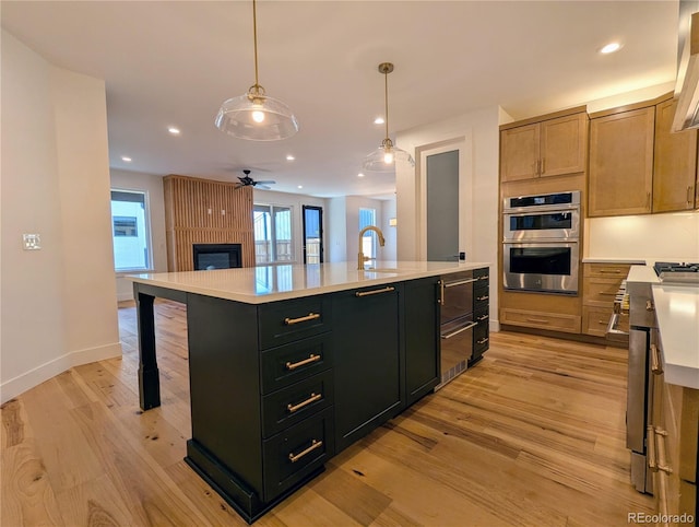 kitchen with light brown cabinets, stainless steel double oven, light hardwood / wood-style flooring, pendant lighting, and a center island with sink