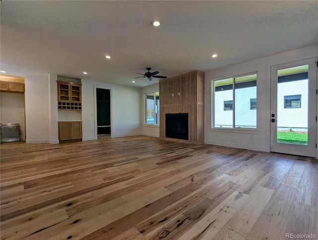 unfurnished living room with a wealth of natural light, a large fireplace, light hardwood / wood-style flooring, and ceiling fan