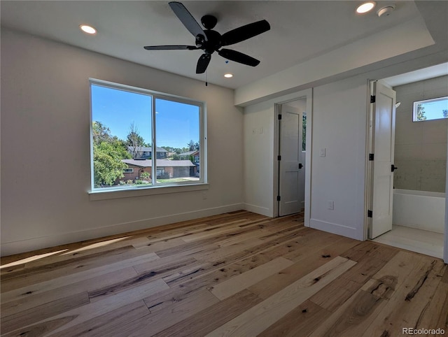 unfurnished bedroom featuring multiple windows, light hardwood / wood-style flooring, ensuite bath, and ceiling fan