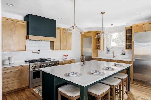 kitchen featuring hanging light fixtures, wall chimney range hood, a kitchen island with sink, and premium appliances