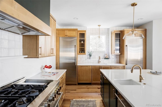 kitchen with island range hood, a sink, high quality appliances, glass insert cabinets, and pendant lighting