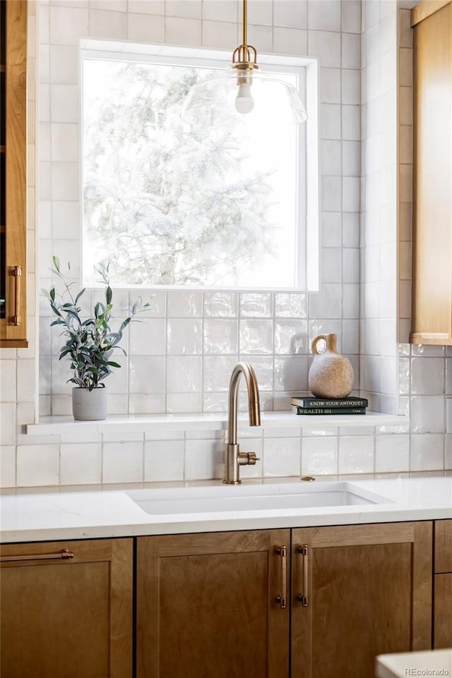 kitchen featuring hanging light fixtures, decorative backsplash, brown cabinetry, and a sink