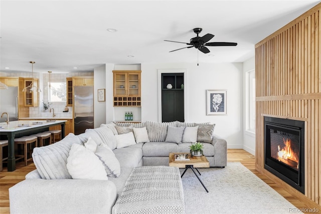 living room featuring light wood-style flooring, ceiling fan, a glass covered fireplace, and recessed lighting