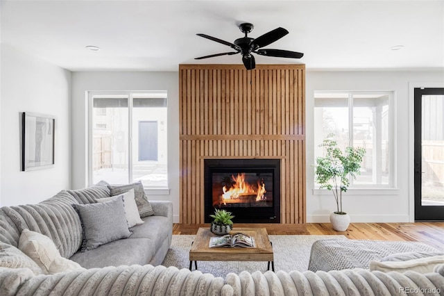 living room featuring a wealth of natural light, a glass covered fireplace, baseboards, and wood finished floors