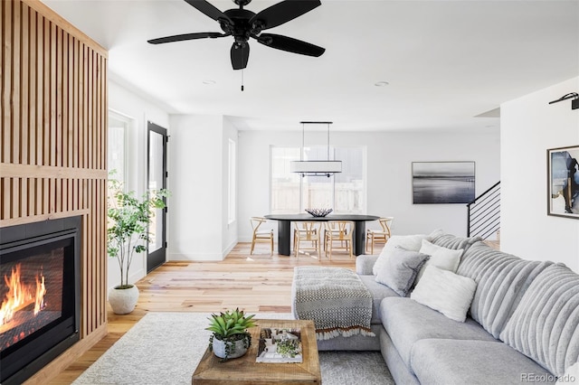 living room featuring stairway, light wood-style flooring, baseboards, and a glass covered fireplace