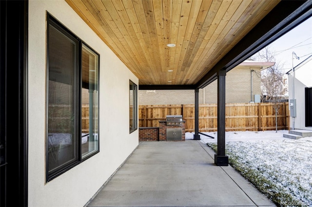 snow covered patio featuring an outdoor kitchen, fence, and a grill