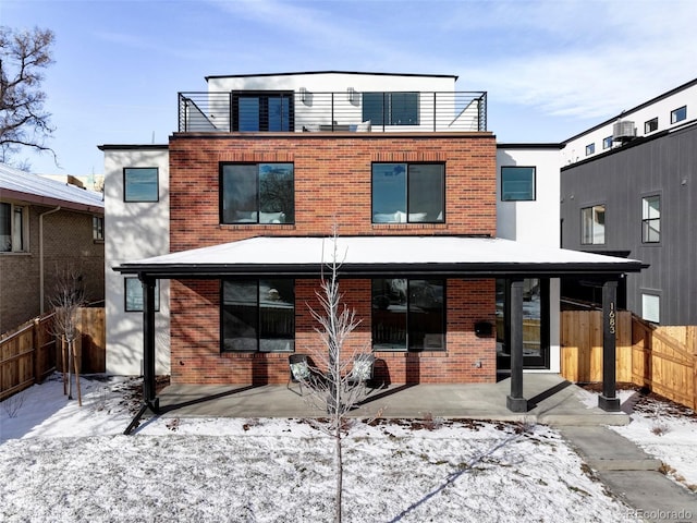 snow covered property featuring a patio area, brick siding, and fence