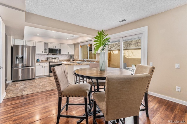 dining room with a textured ceiling, recessed lighting, wood finished floors, visible vents, and baseboards