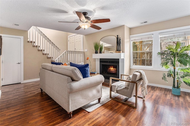 living area with stairs, visible vents, a lit fireplace, and wood finished floors