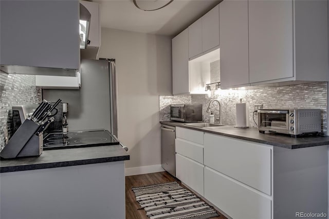 kitchen with a toaster, backsplash, dark countertops, dark wood finished floors, and stainless steel appliances