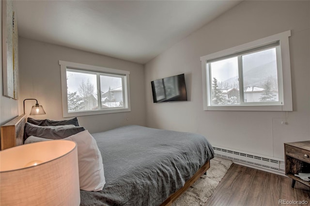 bedroom featuring a baseboard heating unit, vaulted ceiling, and wood finished floors